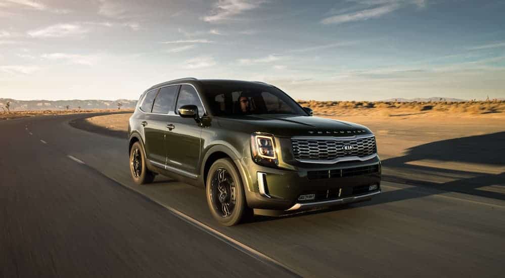 A dark green 2020 Kia Telluride, a popular model at Kia dealership locations, is driving on a road through the desert. 