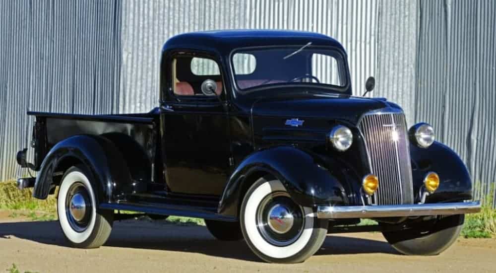 A black 1937 Chevy half-ton pickup truck is parked in front of a metal wall.