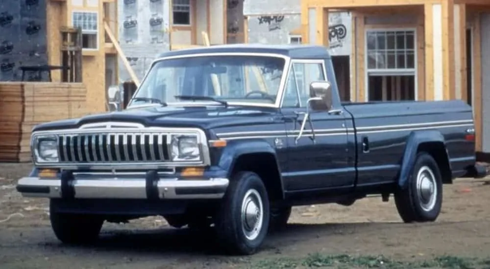 A blue 1987 J Series truck, a favorite among used Jeep trucks, is parked at a construction site. 