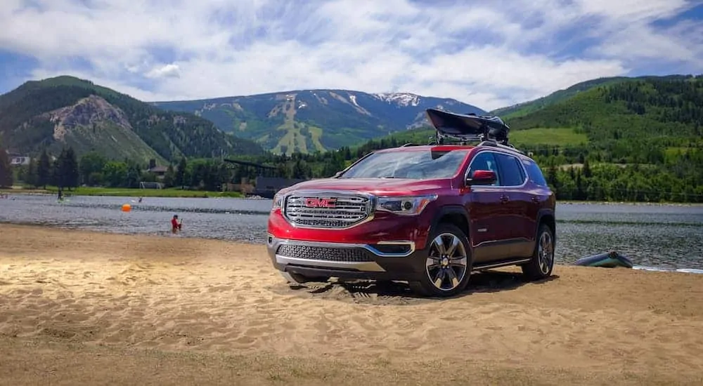 A red 2018 GMC Acadia, which is popular among used SUVs for sale, is parked next to a lake.