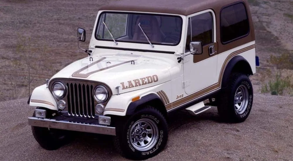 A white Jeep CJ-7 Laredo is parked in a dirt pit with a brown hard top. 