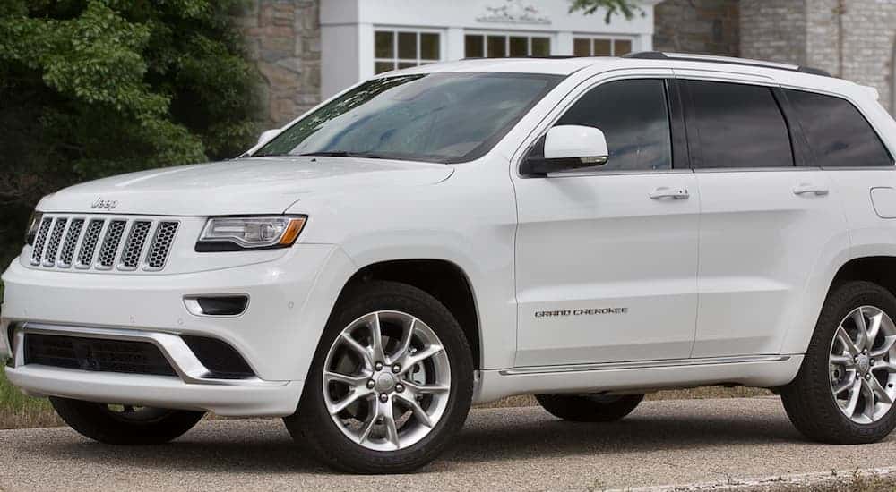 A white 2015 Jeep Grand Cherokee is parked in front of a house.