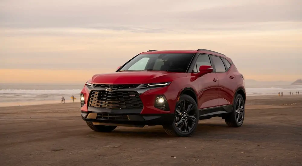 A red 2020 Chevy Blazer RS is parked on a beach with a sun set in the distance. 