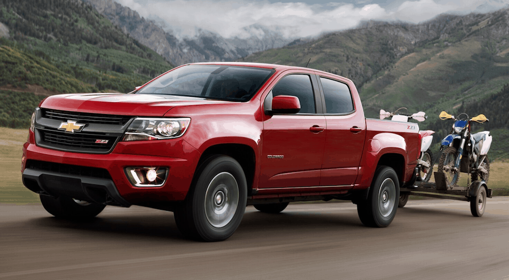 A red 2020 Chevy Colorado is towing two dirt bikes on a trailer with mountains in the background.