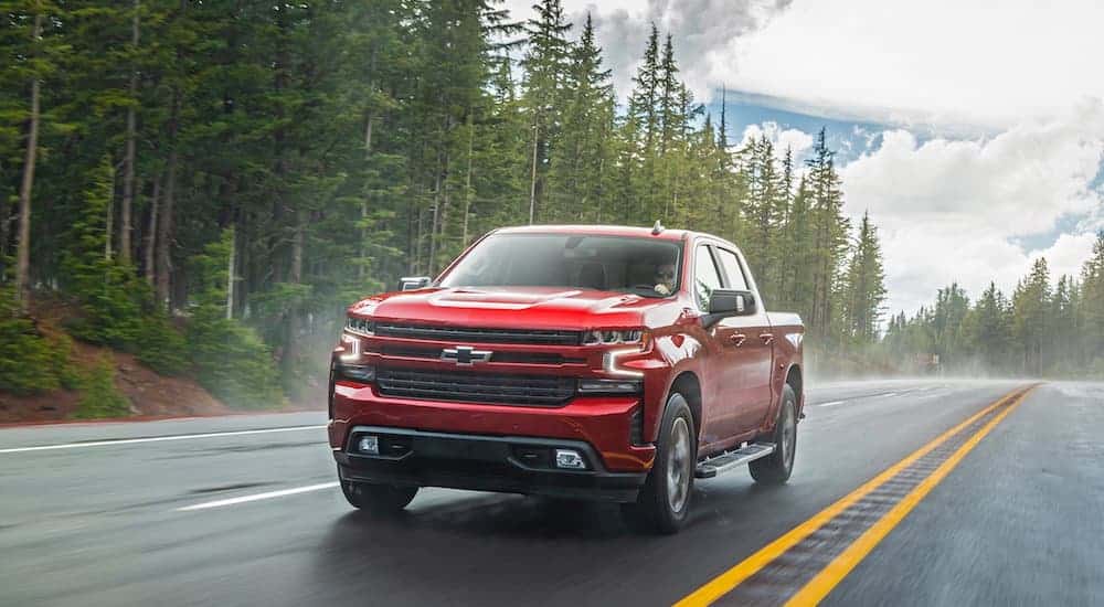 A red 2020 Chevy Silverado 1500 is driving on a treelined road. 