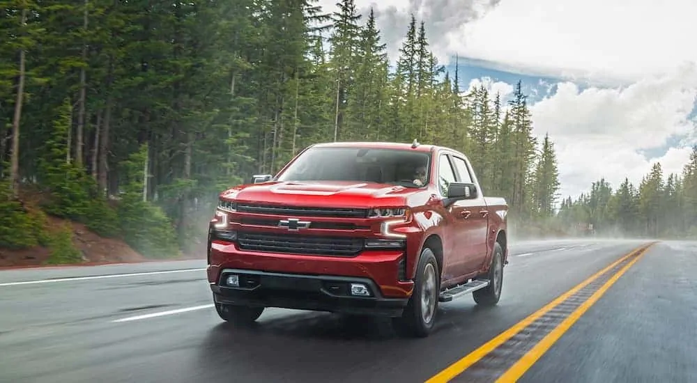 A red 2020 Chevy Silverado 1500 is driving on a treelined road. 
