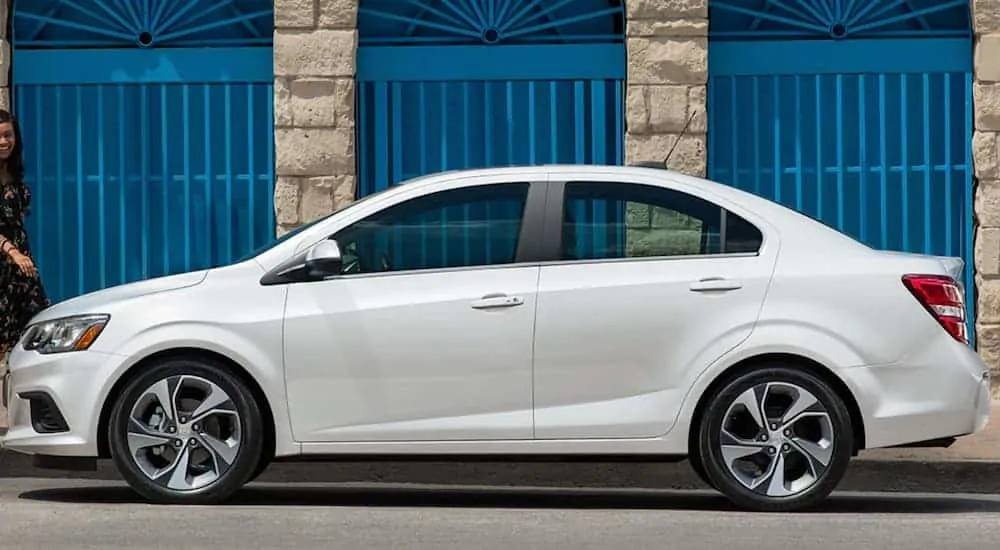 A white 2019 Chevy Sonic is parked on the side of a street next to a concrete building. 