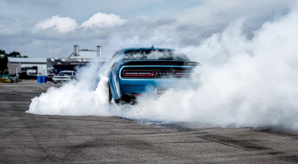 A blue 2020 Dodge Challenger from behind is doing a burnout on a track.