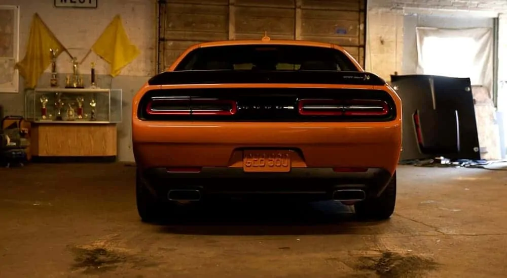 An orange 2020 Dodge Challenger from behind is parked in a garage.