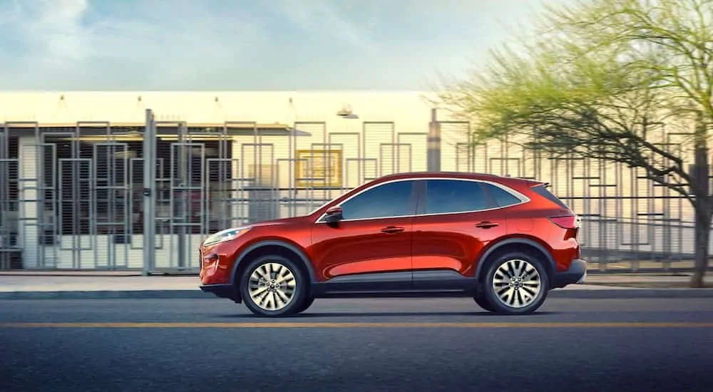 A side view of the all-new red 2020 Ford Escape driving on a city street past buildings. 