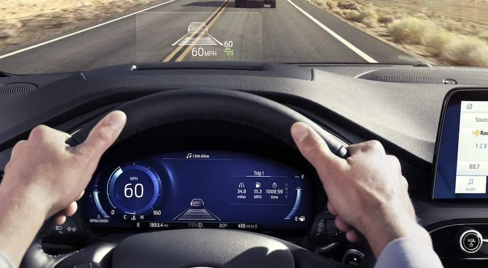 Hands are on the wheel of a 2020 Ford Escape with a drivers display and a Heads-Up display shown on the windshield. 