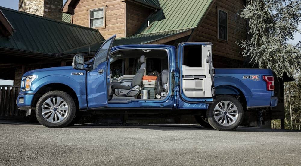 A blue 2020 Ford F-150 is parked in front of a cabin with all the doors open.