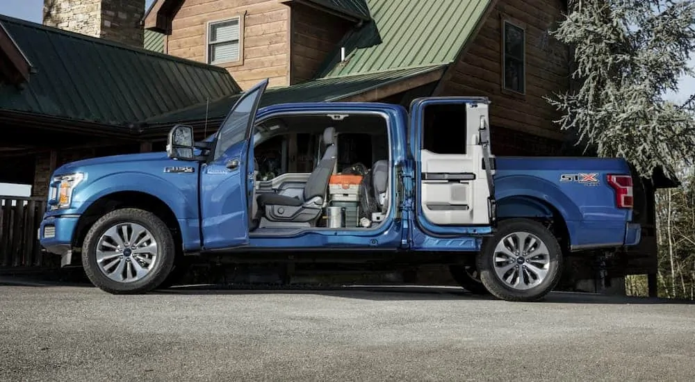 A blue 2020 Ford F-150 is parked in front of a cabin with all the doors open.