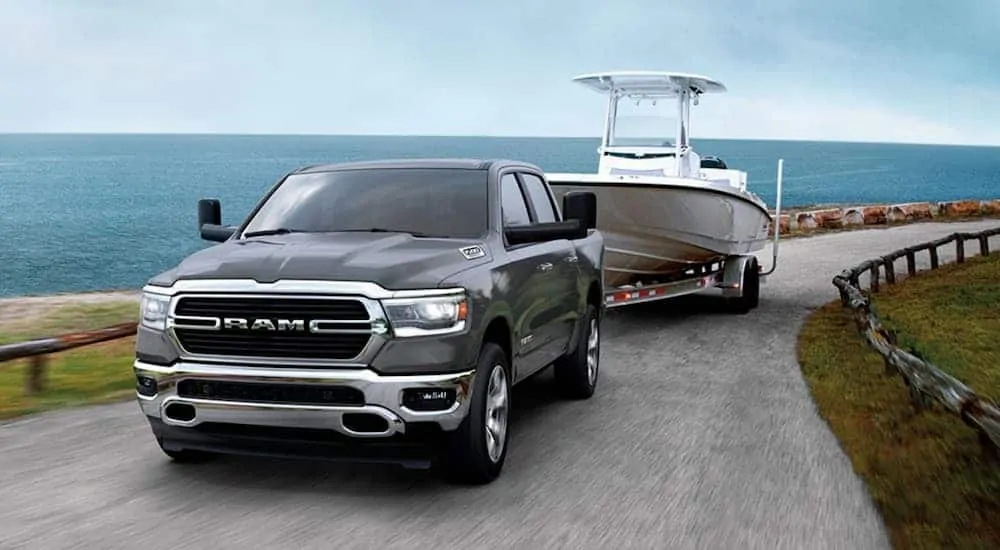 A grey 2020 Ram 1500 is towing a boat uphill near the ocean.