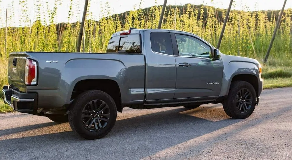 A side view of the 2020 GMC Canyon SLE that's parked on a dirt trail near a grassy field.