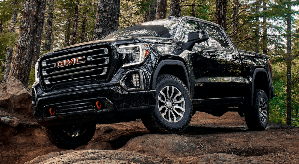 A black 2020 GMC Sierra 1500 AT4 is driving over a rock pile in the woods. 