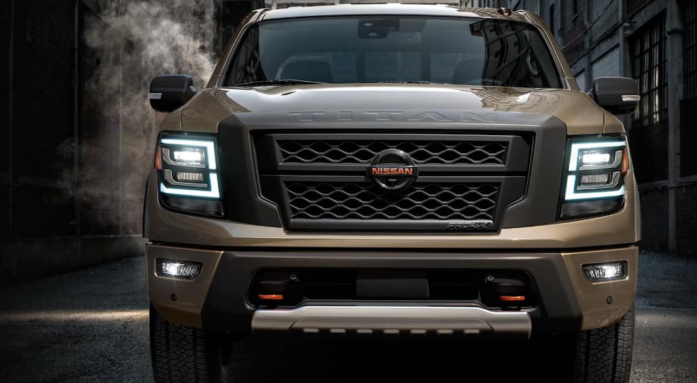A tan 2020 Nissan Titan is parked in a dark alley with the head lights on.