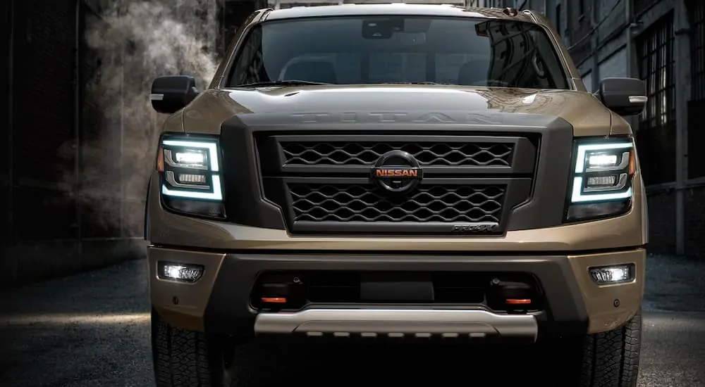 A tan 2020 Nissan Titan is parked in a dark alley with the head lights on.