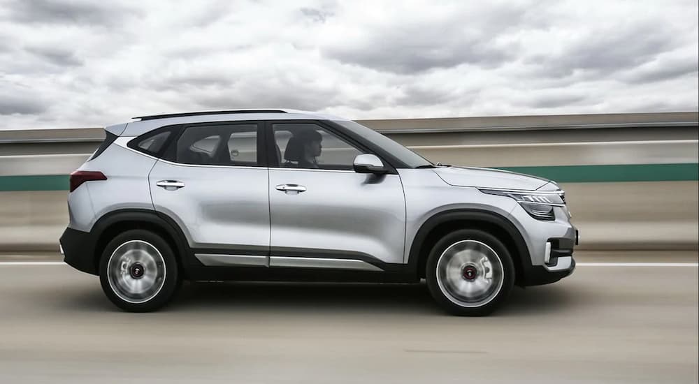 A silver 2020 Kia Seltos is shown from the side while driving on a highway with storm clouds overhead. 