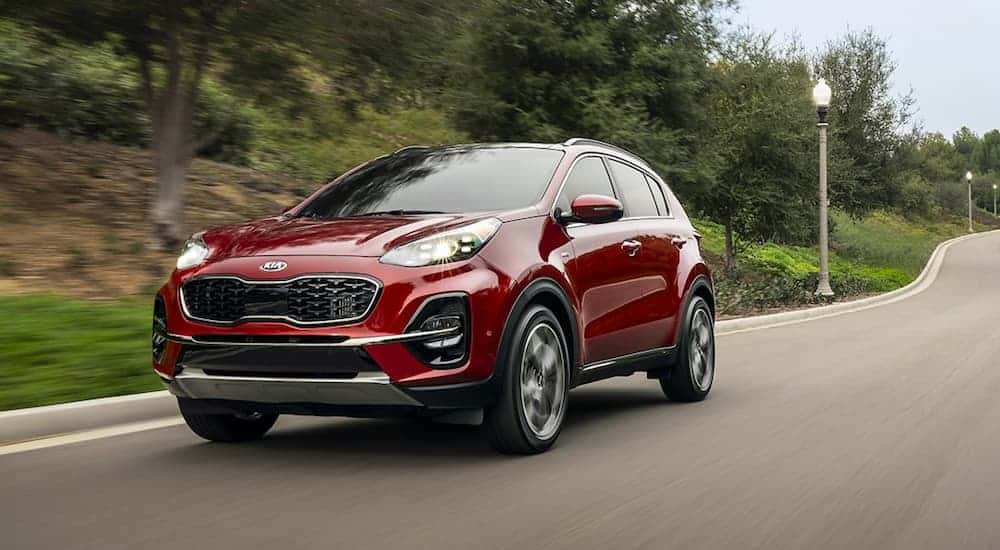 A red 2020 Kia Sportage is driving on a road past blurred trees.