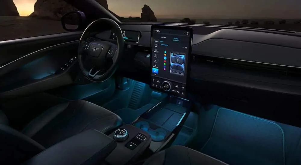 The front black leather interior of a 2021 Ford Mustang Mach-E is lit up with blue accents lights at night.