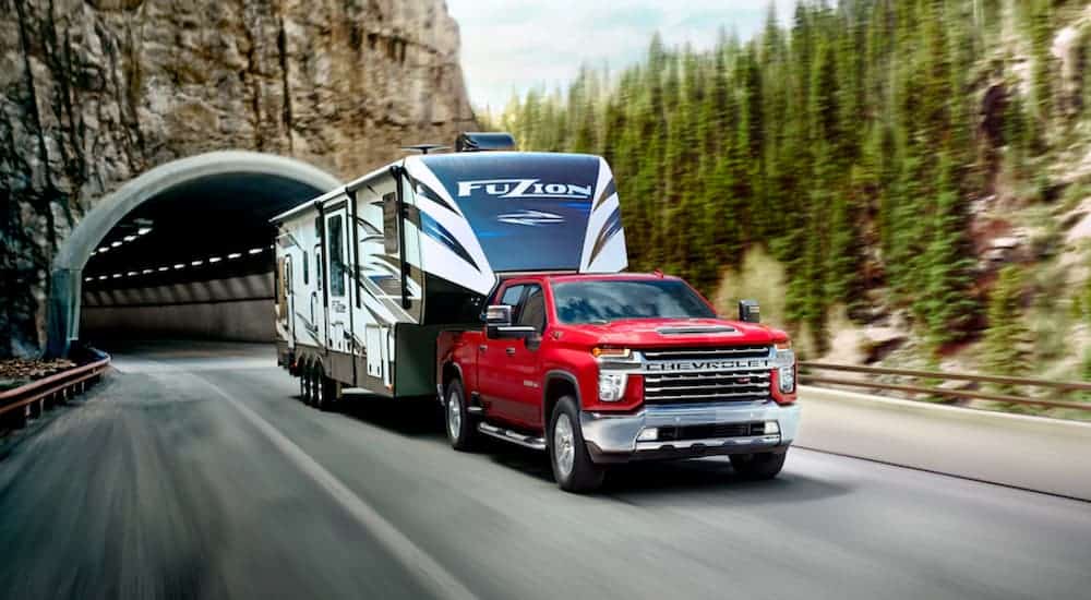 A red 2020 Chevy Silverado HD is towing a camper out of a tunnel. 