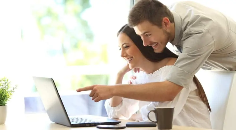 A smiling couple is searching 'GMC dealer near me' on their laptop.