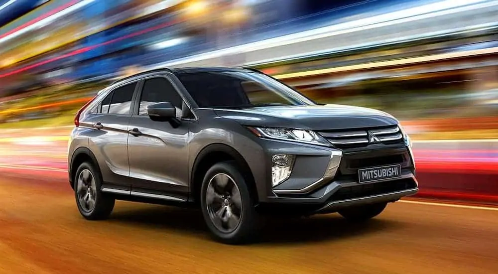 A grey 2020 Mitsubishi Eclipse Cross is driving past blurred city lights at night after leaving a Mitsubishi dealer. 