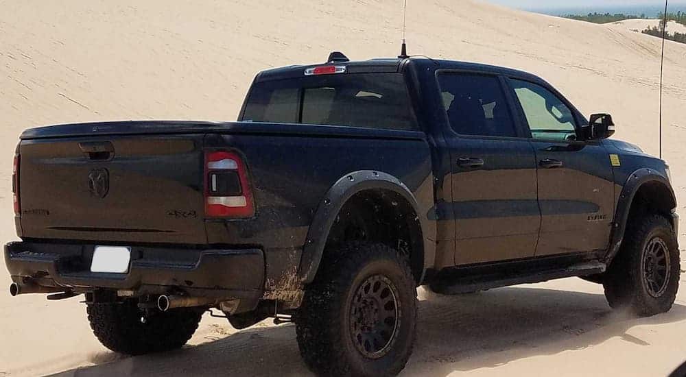 A black lifted Ram 1500 driving away on a sandy dune