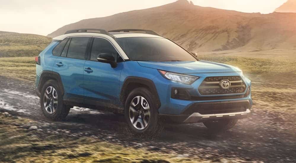 A blue and white 2020 RAV4, which is a popular model at a Toyota dealership near you, is parked on a dirt trail at dusk. 