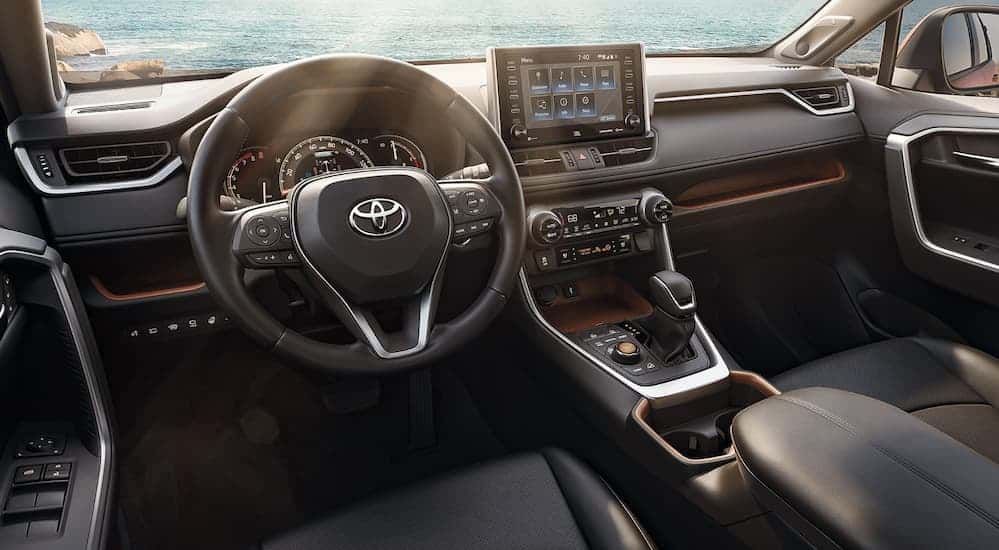 The black leather front interior of a 2020 Toyota RAV4 is shown with a sun glare coming through the windshield. 