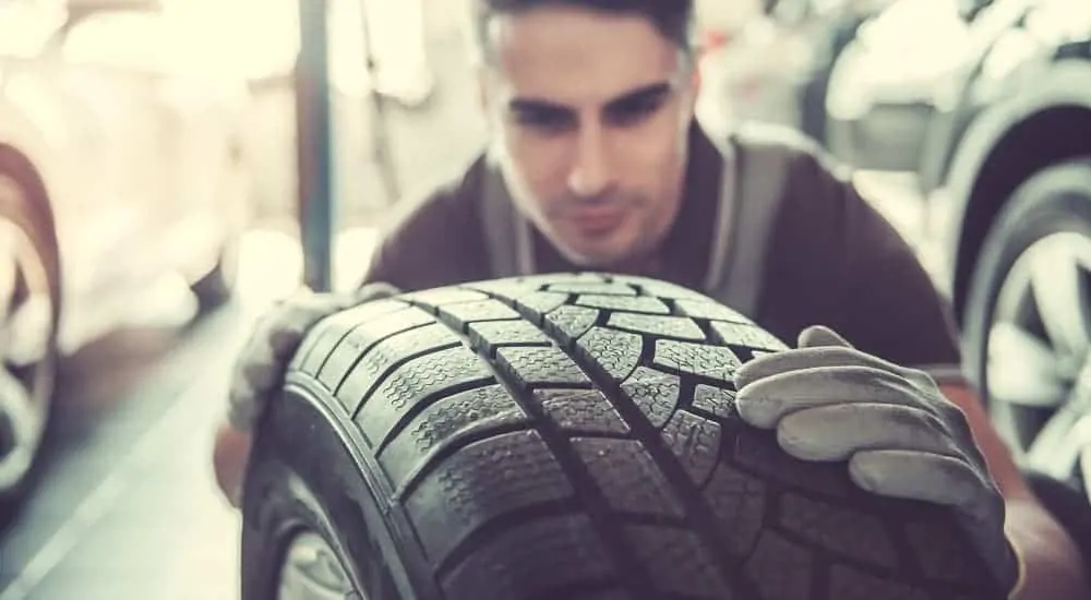 A mechanic at a used car dealer is inspecting a car's tire. 