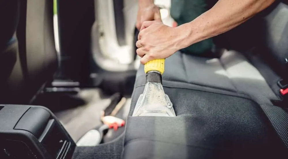 A professional auto detailer is shampooing a customer's car seats. 