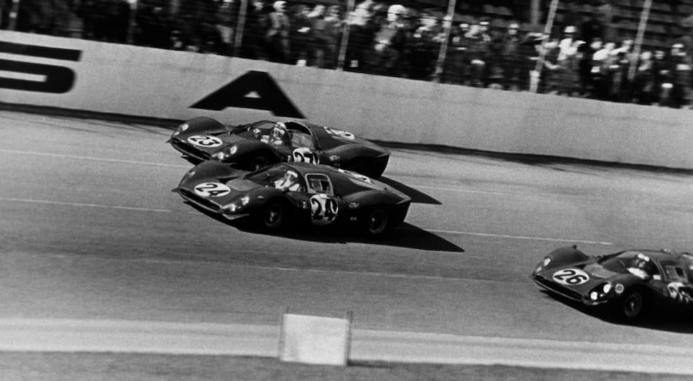 Three 1960s Ferrari race cars are on a racetrack in black and white. 
