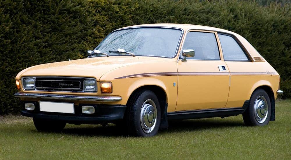 A yellow 1979 Austin Allegro is parked on grassy next to trees. 