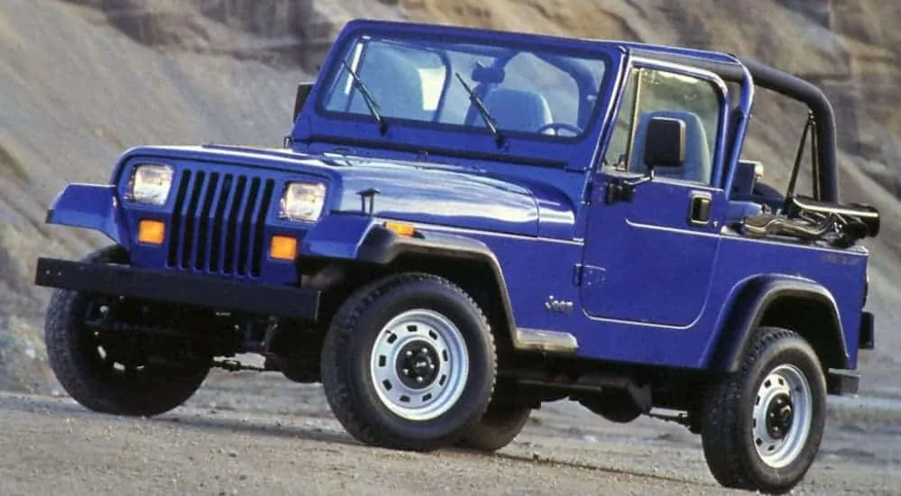 A blue 1990 Jeep YJ is parked on a dirt trail.