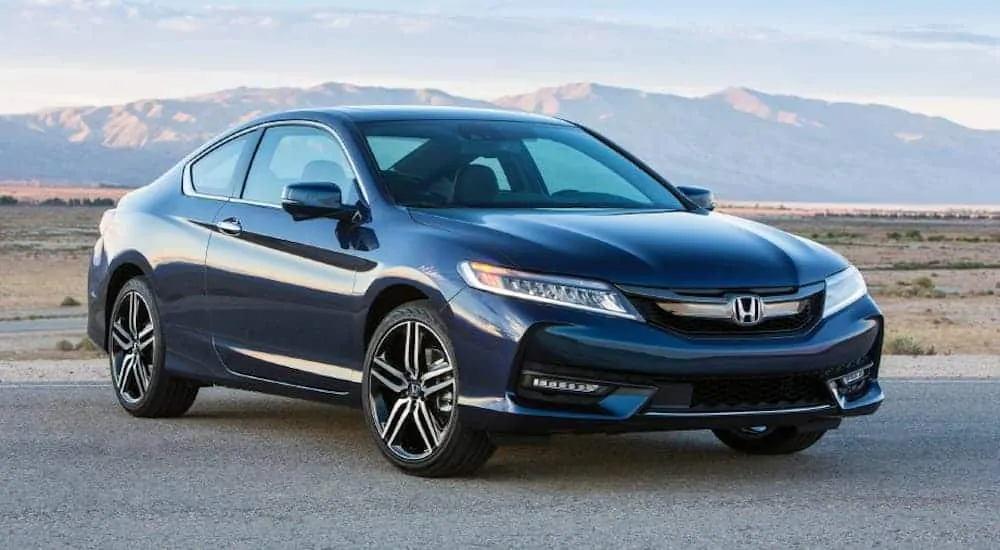 A blue 2016 Honda Accord Coupe is parked on pavement with mountains in the distance. 