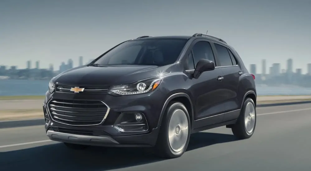 A black 2020 Chevy Trax is driving on a highway with a city skyline in the distance. 