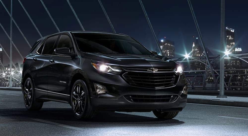 A black 2020 Chevy Equinox, which wins when comparing the 2020 Chevy Equinox vs 2020 Honda CR-V, is driving on a dark lit bridge at night. 
