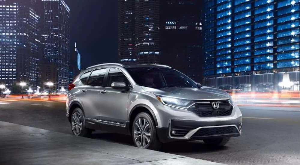 A silver 2020 Honda CR-V is parked on the side of a busy city street at night. 
