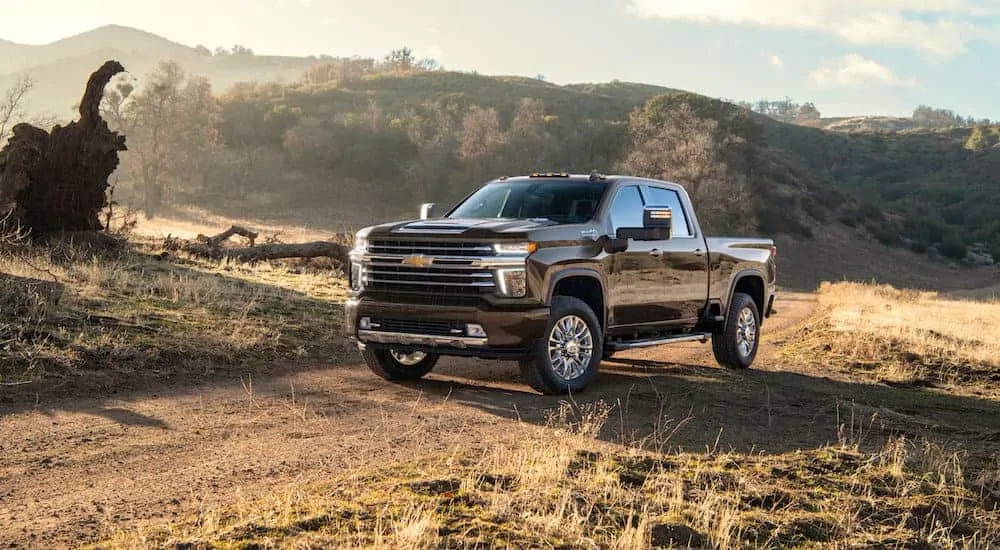 A black 2020 Chevy Silverado 2500HD High Country is parked on a dirt trail with hills in the distance. 