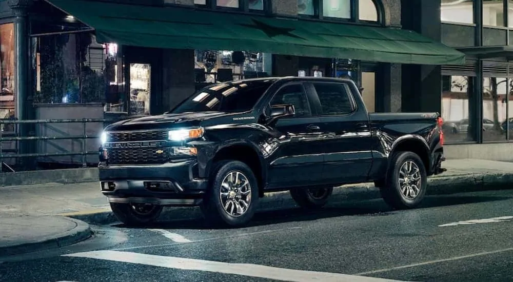 A black 2020 Chevy Silverado 1500 Custom, which wins when comparing the 2020 Chevy Silverado vs 2020 Ford F-150, is parked in front of a store front at night. 