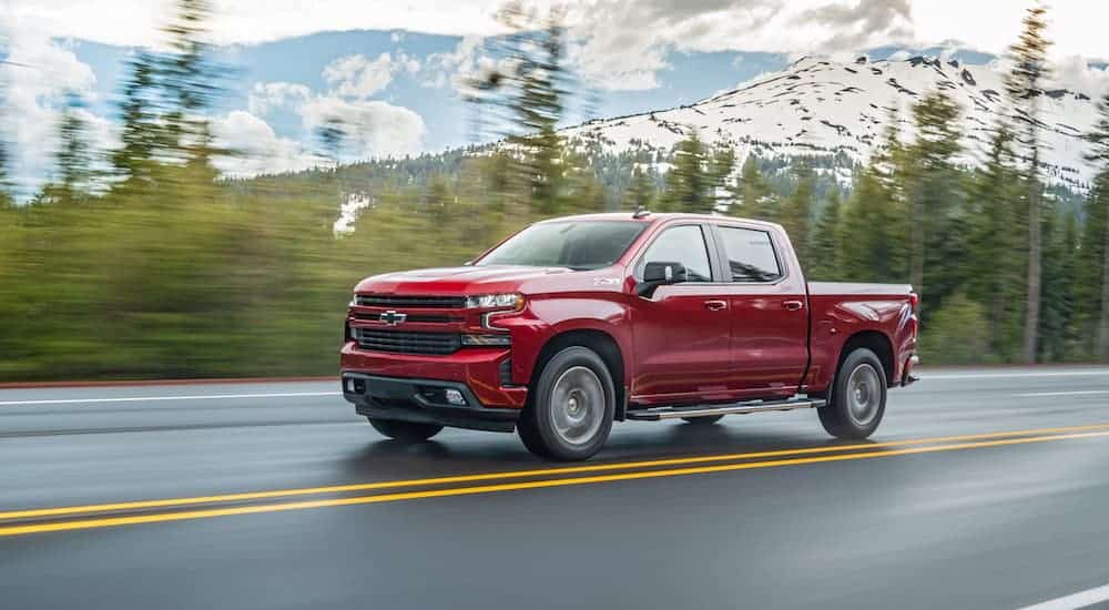 A red 2020 Chevy Silverado 1500 is driving on a wet tree lined road. 