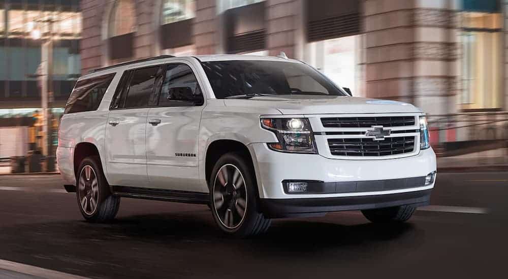 A white 2020 Chevy Suburban is driving through a city at night past blurred buildings. 