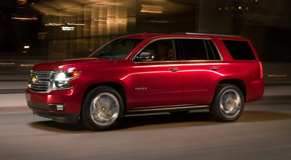 A red 2020 Chevy Tahoe, which is a popular option among Chevy SUVs, is driving on a dark lit street at night. 