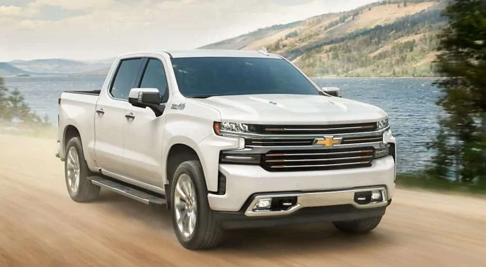 A white 2020 Chevy Silverado 1500 is driving on a dirt road next to a large lake. 