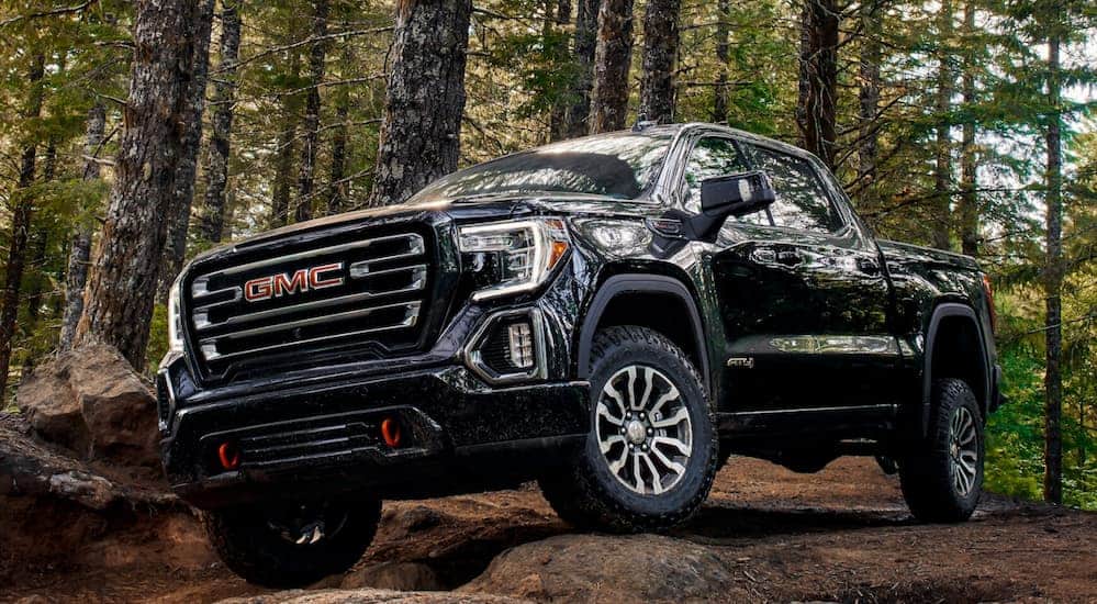 A black 2020 GMC Sierra 1500 AT4, which wins when comparing the 2020 GMC Sierra 1500 vs 2020 Toyota Tundra, is driving on to a large rock in the middle of the woods.