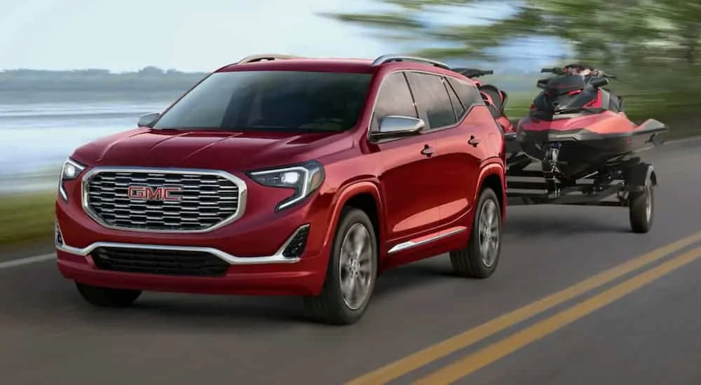 A red 2020 GMC Terrain is towing two jet skies next to a lake.