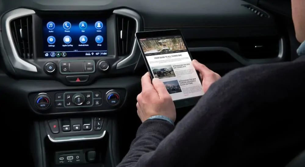 A man is using 4G LTE WiFi on his iPad with the GMC Terrain's infotainment system in front of him.