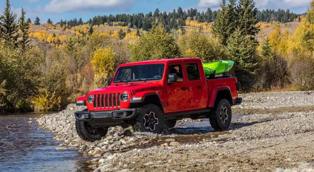 A red 2020 Jeep Gladiator, which is a popular option among modern Jeep models, is driving on rocks next to a river. 